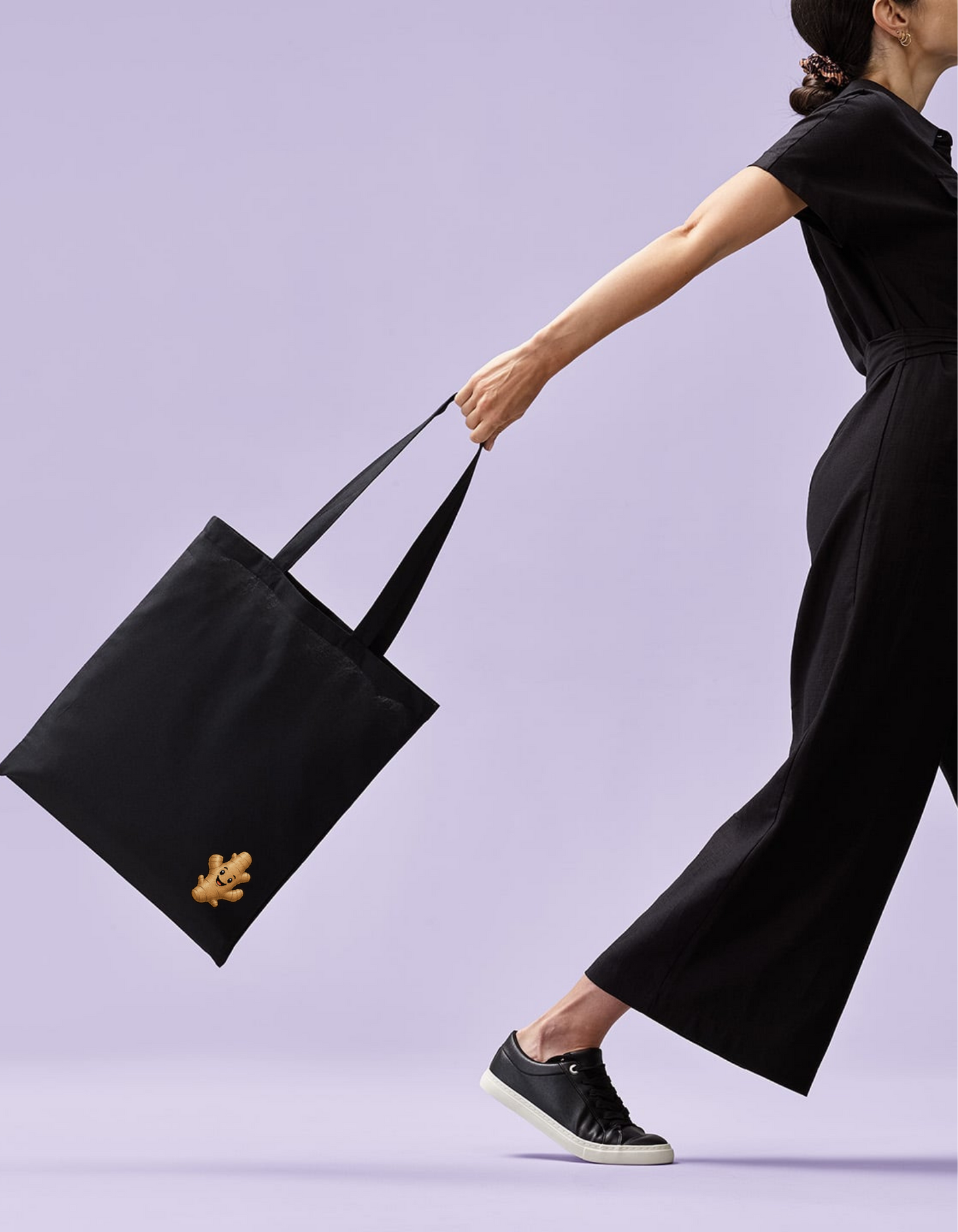 Woman holding a black tote bag with a small logo on a light purple background